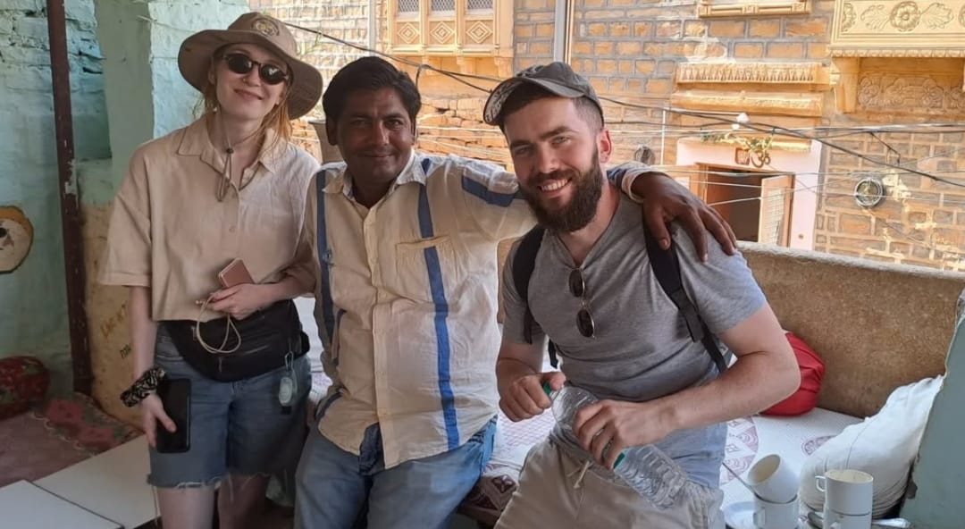 Three people sitting together with carved sandstone façades visible behind them in Jaisalmer.