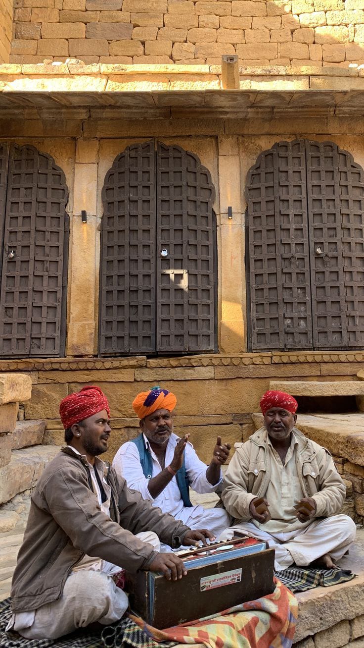 Rajasthani folk musicians performing with a harmonium outside a sandstone building