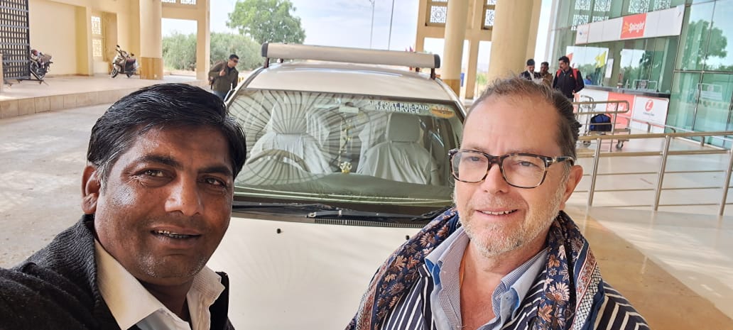 Two people standing beside a white travel vehicle at a transport terminal.