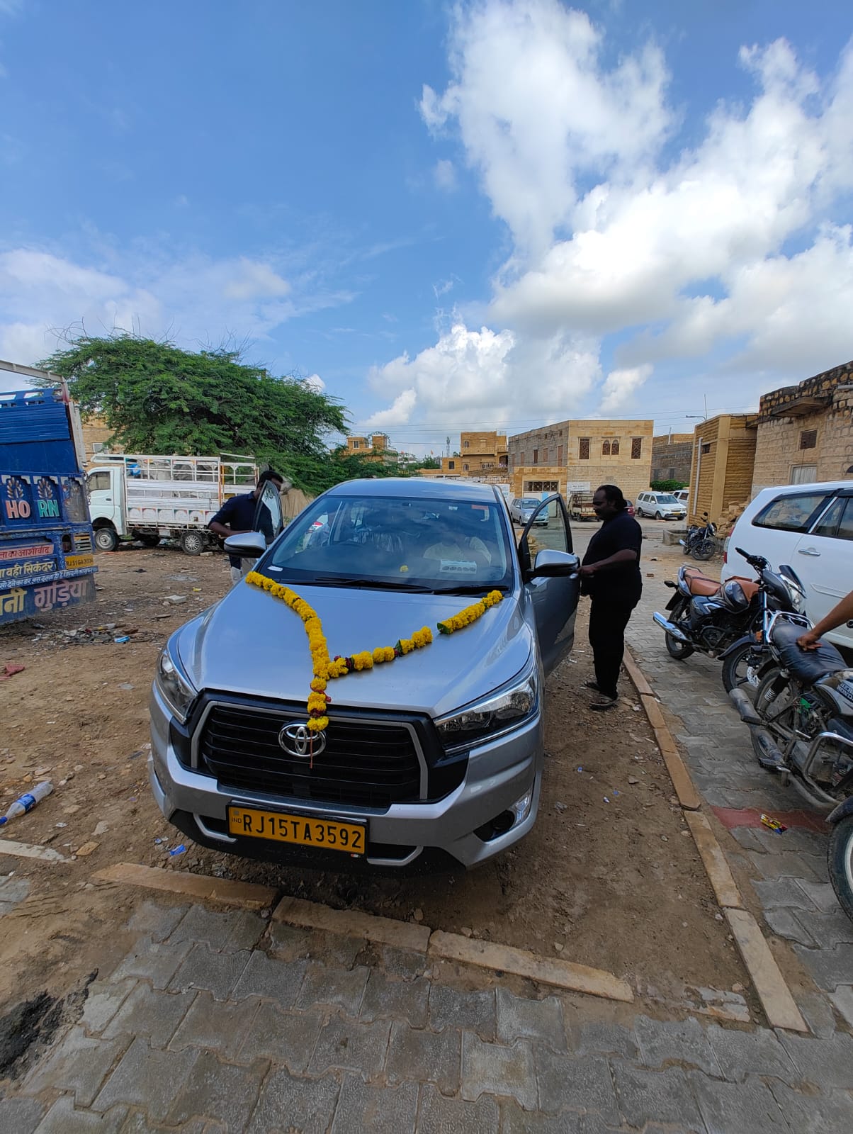 A silver travel vehicle decorated with a flower garland on a street in Jaisalmer.