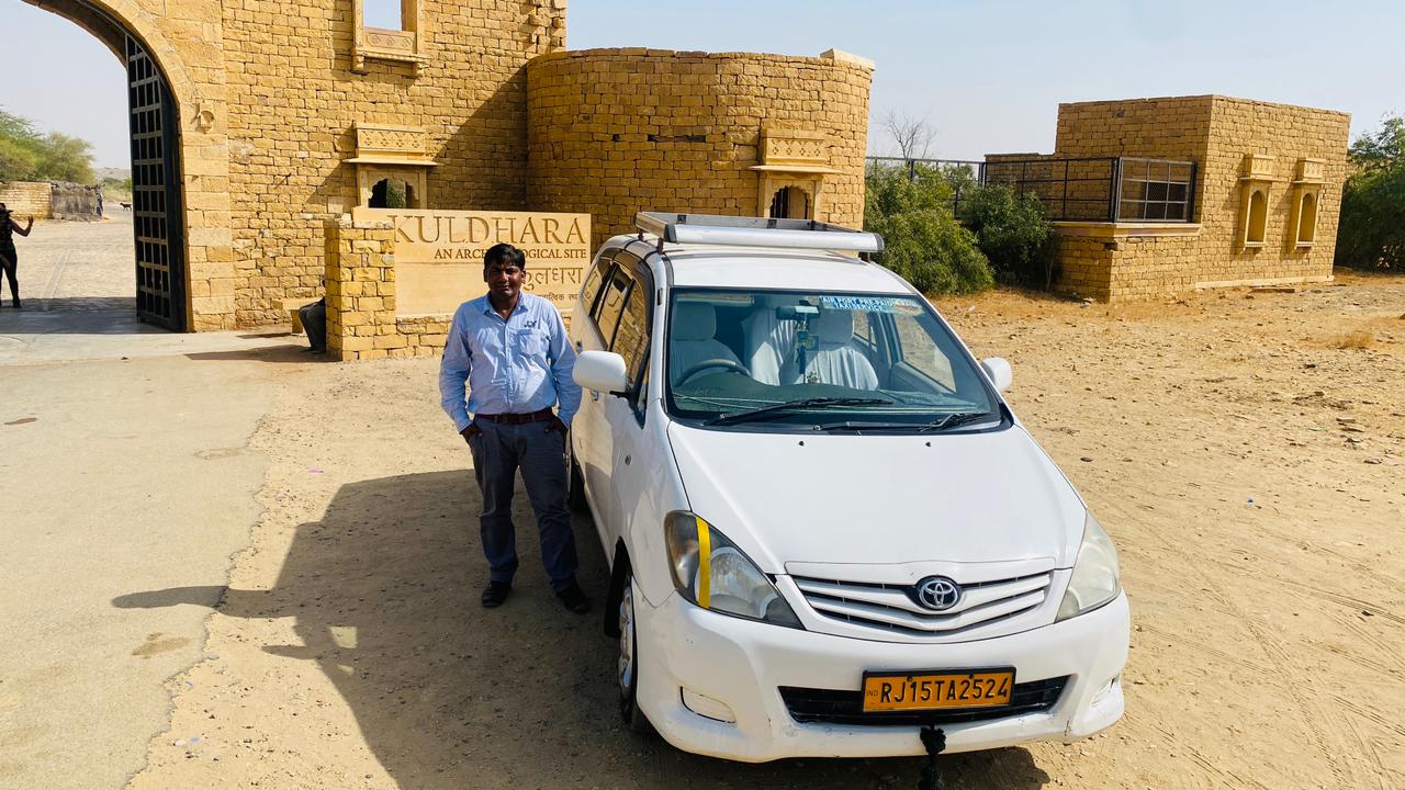 A person standing beside a white travel vehicle outside the Kuldhara archaeological site near Jaisalmer.