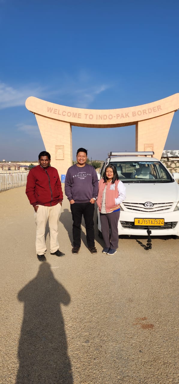 Three people standing beside a vehicle beneath a sign welcoming visitors to the Indo-Pak border.