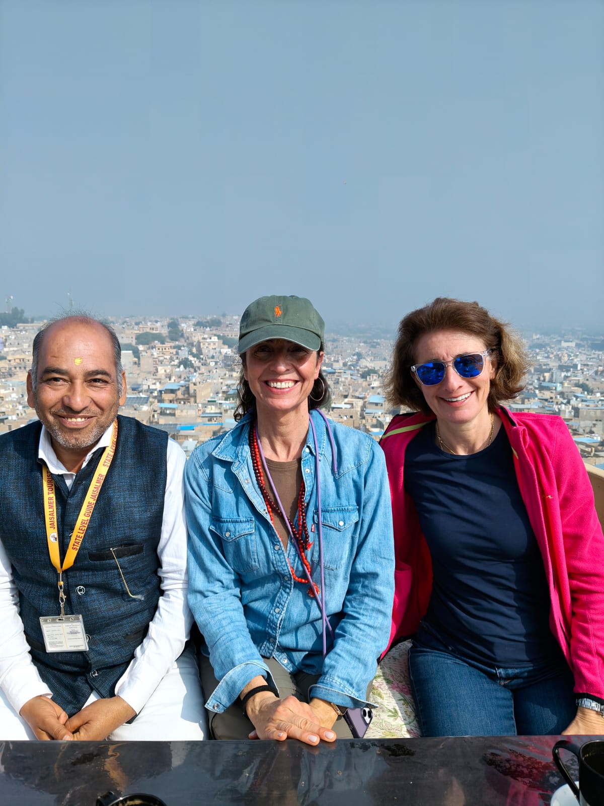 Three people sitting together with Jaisalmer visible in the background.